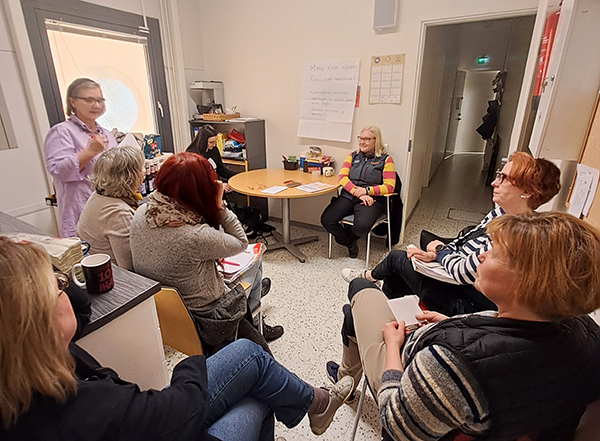 Kuusi henkilöä istuu toimistohuoneessa kuuntelemassa seisoen puhuvaa Annu Niskasta. 